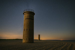 World War II observation towers at Cape Henlopen State Park in Delaware under a starry night sky, with soft sand dunes and a distant horizon glow.